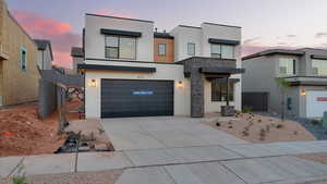 Contemporary house featuring stucco siding, a garage, driveway, and stone siding