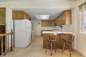 Kitchen featuring white appliances, brown cabinets, a peninsula, and light countertops