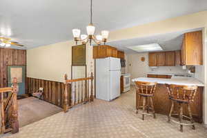 Kitchen featuring white appliances, light colored carpet, light countertops, a peninsula, and brown cabinetry