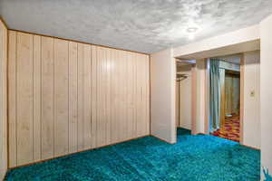 Unfurnished bedroom featuring carpet, wooden walls, and a textured ceiling