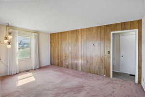 Unfurnished bedroom featuring a textured ceiling, wooden walls, and carpet flooring