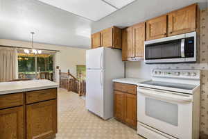 Kitchen featuring white appliances, brown cabinets, light countertops, a chandelier, and decorative light fixtures