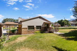 Back of house with brick siding, a lawn, and a chimney