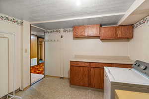Laundry room featuring light floors, cabinet space, a textured ceiling, and washer and clothes dryer