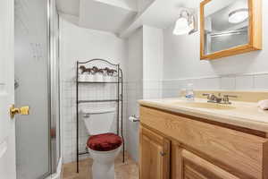 Full bath featuring vanity, a shower stall, tile walls, tile patterned floors, and a wainscoted wall
