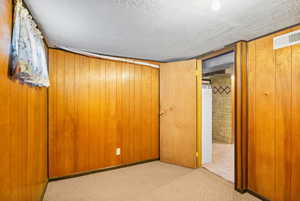 Unfurnished bedroom featuring carpet flooring, a textured ceiling, and wooden walls