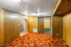 Hallway featuring wooden walls, carpet flooring, and a textured ceiling