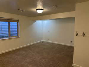 Empty room with a textured ceiling and dark colored carpet