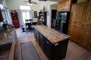 Kitchen with black refrigerator with ice dispenser, light wood finished floors, a ceiling fan, a center island, and light stone counters