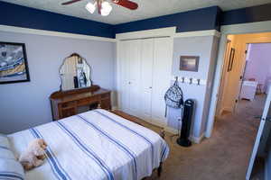 Carpeted bedroom featuring a closet, a ceiling fan, and a textured ceiling