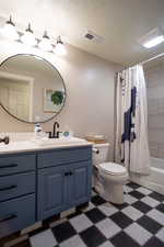 Full bath with vanity, shower / bathtub combination with curtain, dark flooring, and a textured ceiling