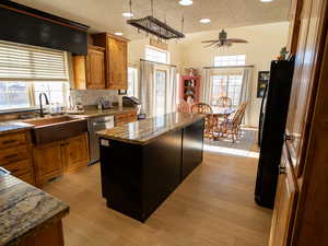 Kitchen with a ceiling fan, brown cabinets, freestanding refrigerator, a kitchen island, and dark stone countertops