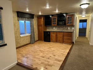 Bar featuring wood finish cabinets, light wood-style floors, a textured ceiling, dark countertops, and light colored carpet