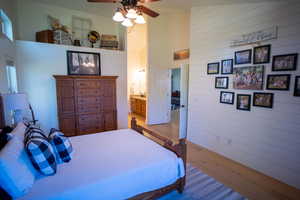 Bedroom featuring wood finished floors, wooden walls, a towering ceiling, and ceiling fan