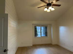 Spare room featuring a ceiling fan, light wood-style flooring, wooden walls, and vaulted ceiling