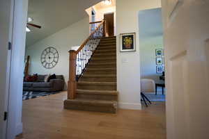 Stairs with wood finished floors, a ceiling fan, and high vaulted ceiling