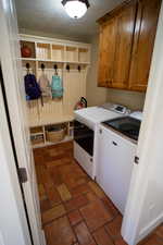 Washroom with washer and clothes dryer, cabinet space, a textured ceiling, and brick flooring