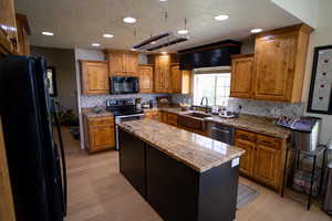Kitchen with black appliances, a textured ceiling, light wood finished floors, brown cabinets, and decorative backsplash