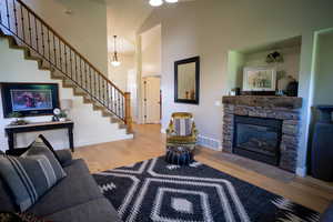 Living area with stairs, wood finished floors, a fireplace, and high vaulted ceiling
