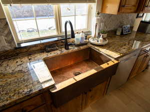 Kitchen with brown cabinetry, dark stone countertops, decorative backsplash, dishwasher, and light wood-style floors
