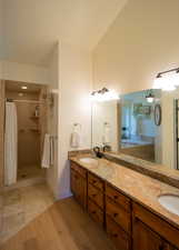 Bathroom featuring a shower stall, double vanity, and light wood finished floors
