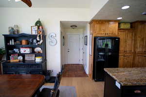Kitchen featuring black refrigerator with ice dispenser, stone counters, brown cabinetry, light wood-style floors, and a textured ceiling