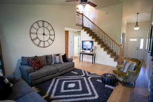 Living area featuring a towering ceiling, stairs, wood finished floors, and ceiling fan
