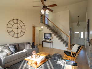 Living room featuring high vaulted ceiling, hardwood / wood-style floors, stairway, and ceiling fan