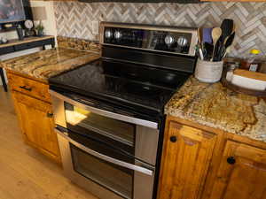 Kitchen featuring brown cabinets, range with two ovens, decorative backsplash, dark stone counters, and light wood finished floors