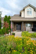View of front of home with a shingled roof, a porch, and stone siding