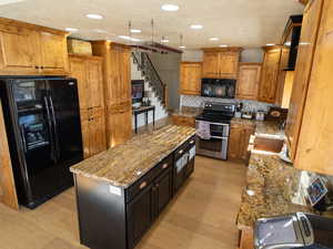 Kitchen featuring light stone counters, black appliances, a center island, brown cabinetry, and recessed lighting