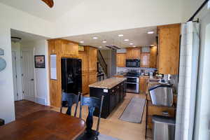 Kitchen with black appliances, decorative backsplash, a kitchen island, recessed lighting, and light stone countertops