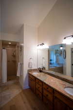 Full bath featuring double vanity, a shower with curtain, wood finished floors, and vaulted ceiling