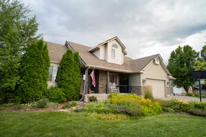 View of front of house featuring covered porch, roof with shingles, a front lawn, and stone siding