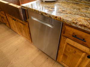 Kitchen view of brown cabinets, dishwasher, dark stone counters, and light wood-type flooring