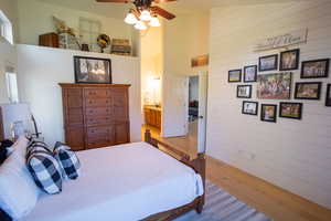 Bedroom featuring a high ceiling, wood finished floors, a ceiling fan, wood walls, and ensuite bath
