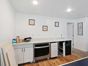 Indoor wet bar featuring oven, beverage cooler, and light wood-style flooring