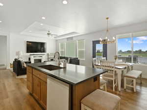 Kitchen featuring a raised ceiling, ceiling fan, white dishwasher, light wood finished floors, and brown cabinetry