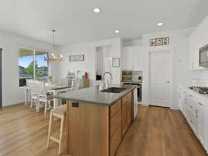 Kitchen featuring a chandelier, light wood finished floors, decorative backsplash, a center island with sink, and recessed lighting