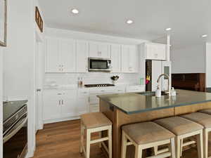 Kitchen featuring a breakfast bar, appliances with stainless steel finishes, dark wood-style floors, white cabinets, and backsplash