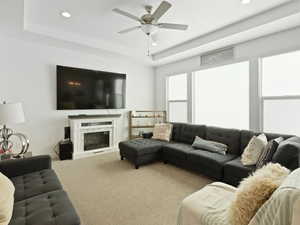 Carpeted living room with a tray ceiling, recessed lighting, a ceiling fan, and a premium fireplace