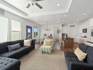 Living room featuring a chandelier, a ceiling fan, recessed lighting, dark wood finished floors, and a tray ceiling