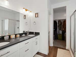 Full bath with a stall shower, double vanity, wood finished floors, and a walk in closet
