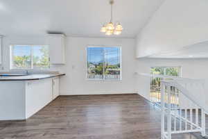 Kitchen featuring a chandelier, dark wood finished floors, white cabinets, vaulted ceiling, and decorative light fixtures