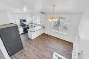 Kitchen featuring a peninsula, a chandelier, stainless steel appliances, white cabinets, and wood finished floors