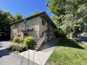 View of side of property with brick siding, a yard, a balcony, and stairs