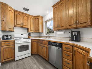 Kitchen featuring white gas stove, dishwasher, brown cabinetry, and recessed lighting