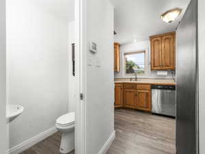 1/2 bathroom near kitchen featuring light wood finished floors, dishwasher, light countertops, and brown cabinets