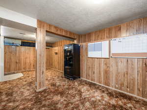 Below grade area with a textured ceiling, wooden walls, and carpet flooring