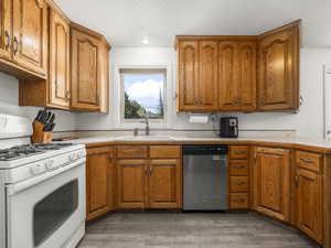 Kitchen with white gas range, dishwasher, brown cabinetry, and a textured ceiling